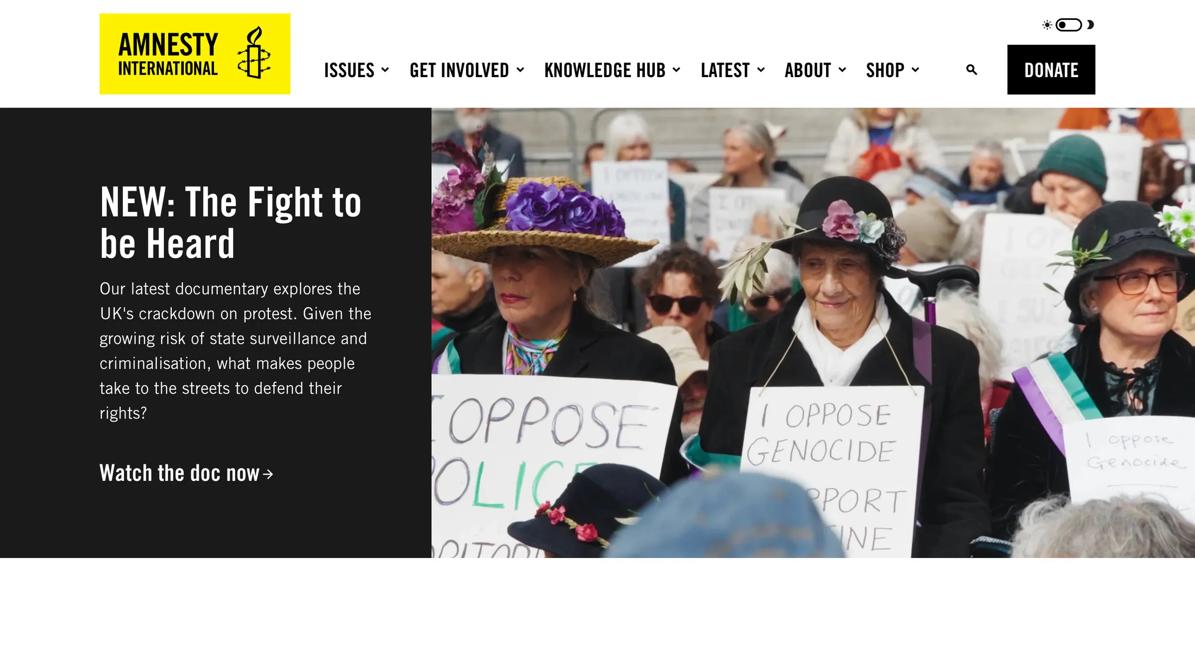Amnesty International UK’s homepage: the yellow Amnesty logo on a black header, a Donate button, and a photo of protesters in bright hats holding placards next to the headline NEW: The Fight to be Heard