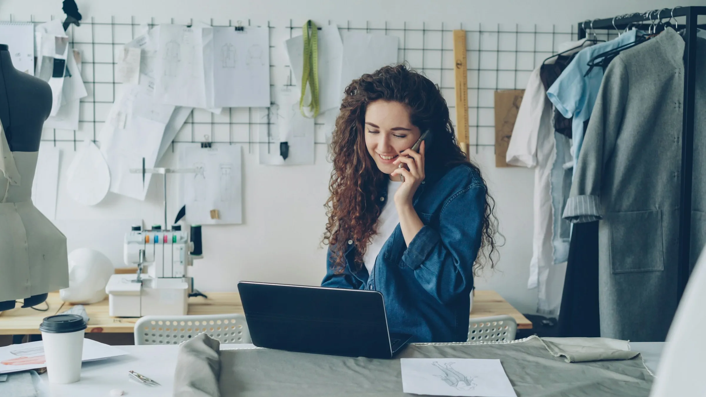 A designer on the phone while working on a laptop in her studio