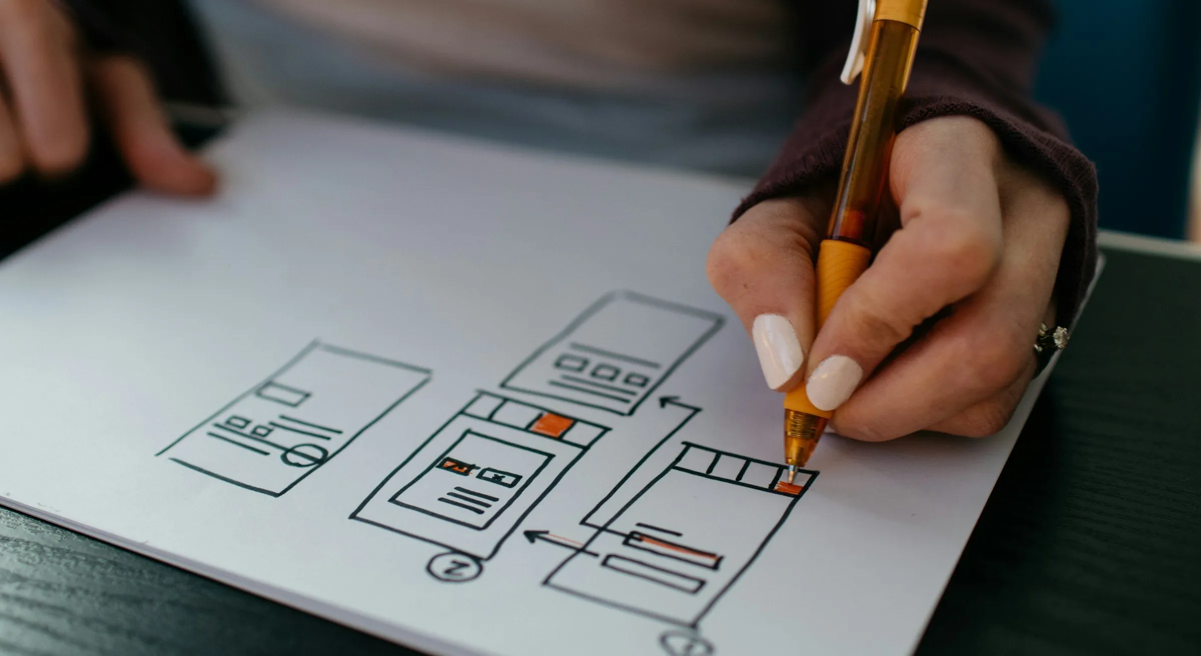 A hand sketching website page layouts on paper with a pen